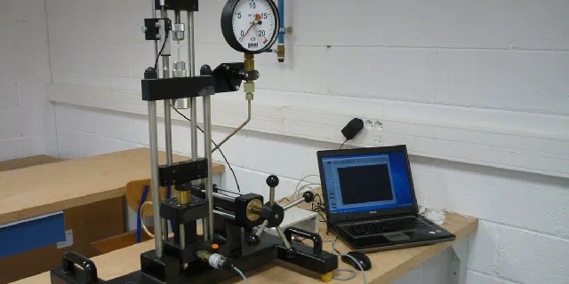 Tensile testing machine with pressure gauge and laptop in a test lab